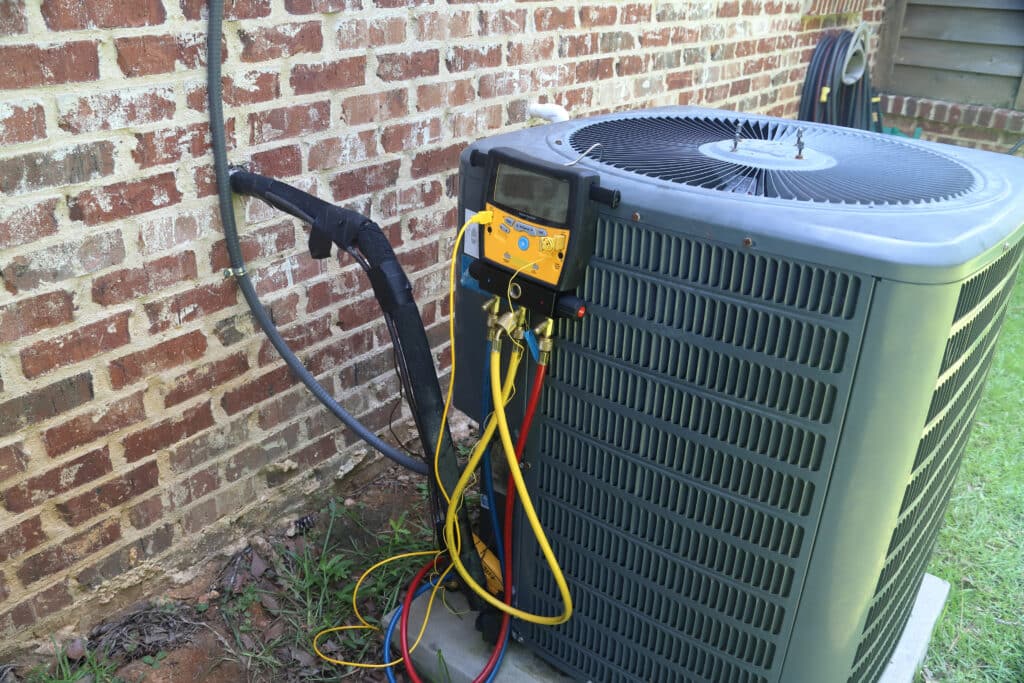 An outdoor residential AC heat pump unit being tested with a digital HVAC service gauge manifold to check for refrigerant levels.