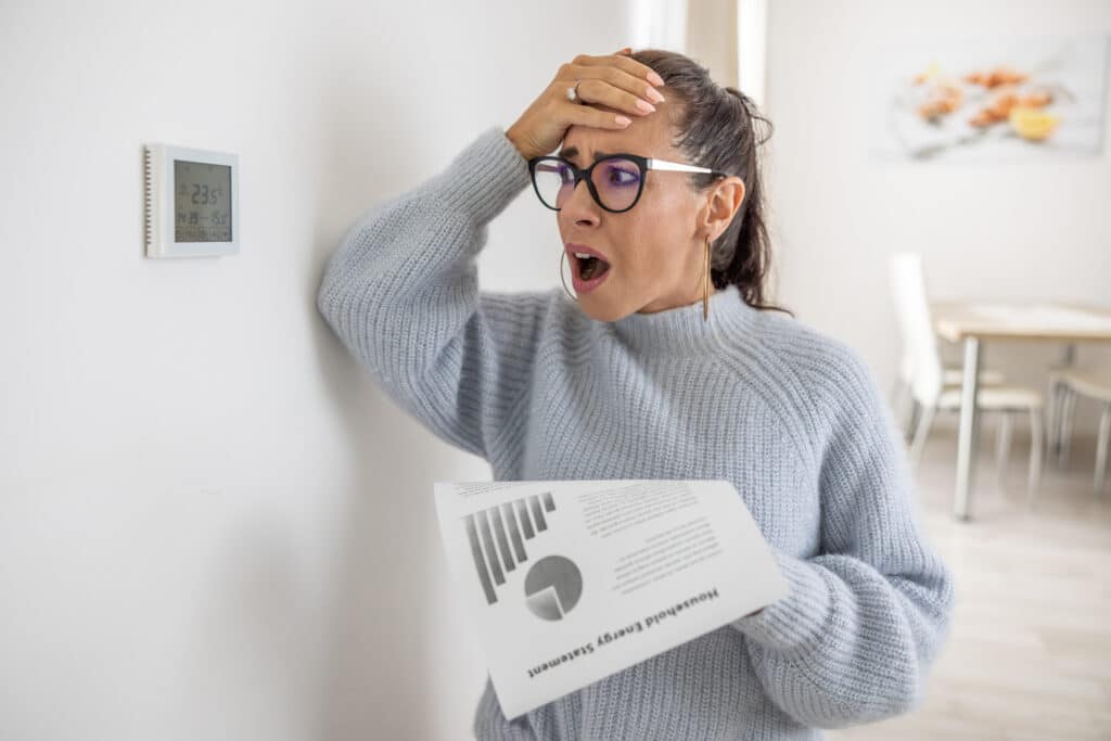 Homeowner looking at thermostat and high heating bill